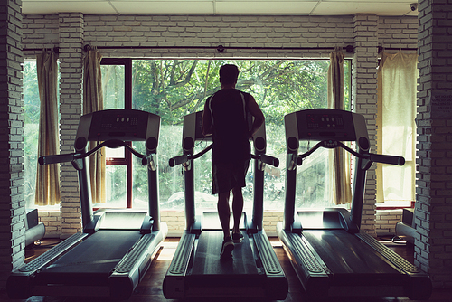 Rear view of sportsman running on threadmill in small local gym