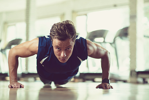 Portrait shot of handsome young athlete  while doing push-ups at spacious gym with panoramic windows