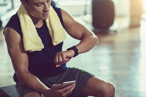 Sporty young man checking smart watch after training in gym