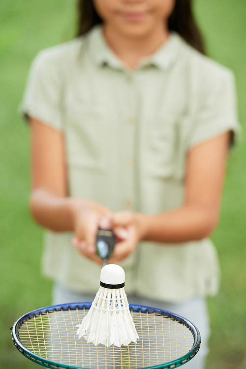 Anonymous girl holding badminton racquet and shuttlecock near camera while standing in park