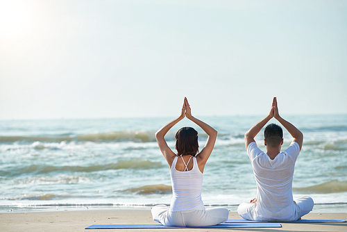 Rear view of young couple enjoying yoga practice on the beach