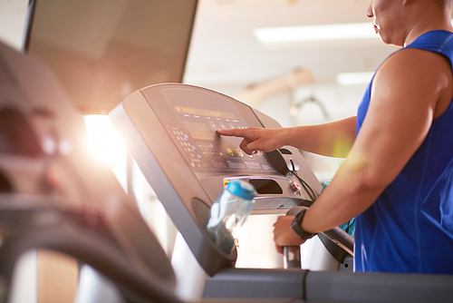 Sporty man choosing program on threadmill before running