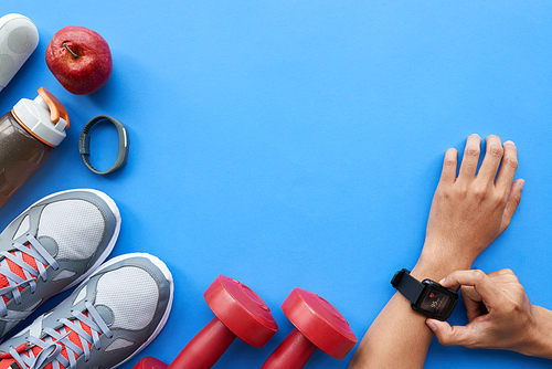 Flat lay of sport equipment and man checking heart rate on his smart watch