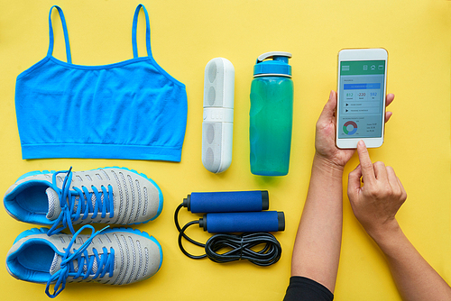 Sportswear and accessories and hands of woman checking smartphone application