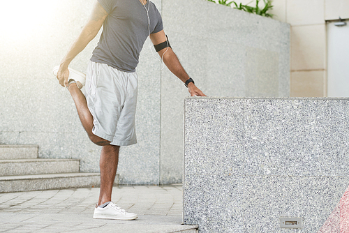 Cropped image of man leaning on granite border and stretching legs after jogging