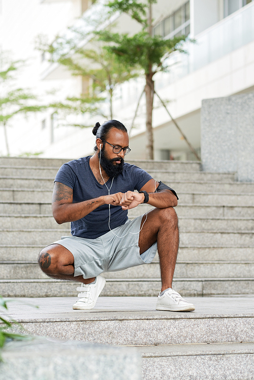 Handsome sporty Indonesian man checking pulse on smartwatch