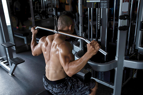 Sweaty fit strong young man doing exercise on pull down machine