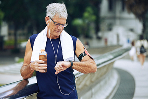 Senior jogger drinking water and checking application on his fitness tracker