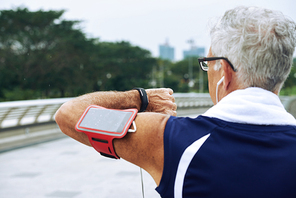 Rear view of elderly runner checking heart rate on fitness tracker when training