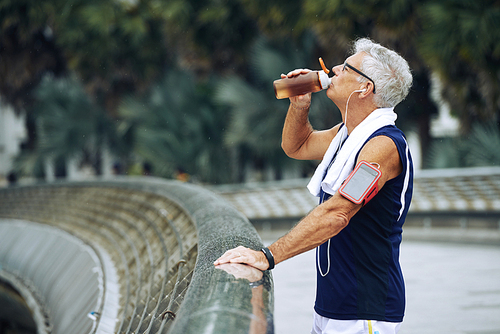 Thirsty elderly jogger drinking water after running in the morning