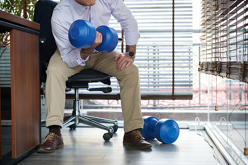 Businessman doing exercises with dumbbells during short break in office