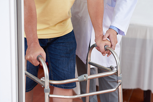Unrecognizable medical practitioner helping man to use walking frame during rehabilitation session in doctor's office