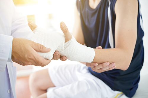 Doctor applying bandage on broked hand of male patient