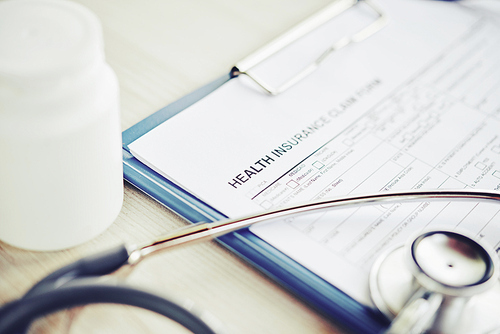 Close-up image of health insurance document, stethoscope and pills