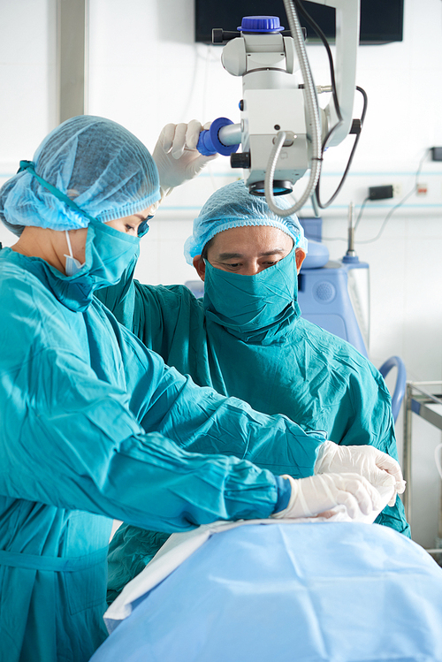 Asian professional man and woman preparing patient for surgery working in team in operating room