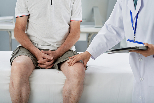 Doctor palpating thigh of senior man during daily check-up