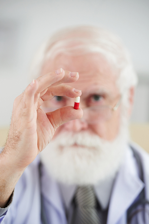 Defocused senior pharmacist holding drug capsule in his hand