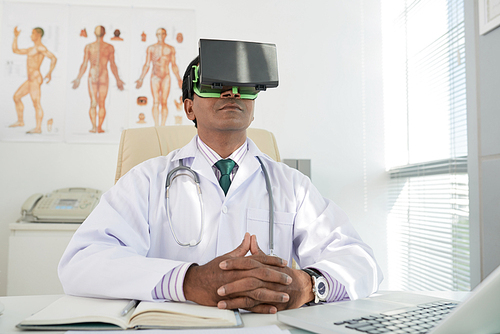 Portrait of Indian doctor in virtual reality headset sitting at his table