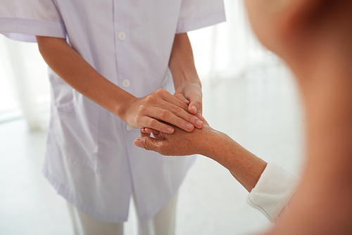 Closeup image of doctor touching hand of aged patient to reassure and support her