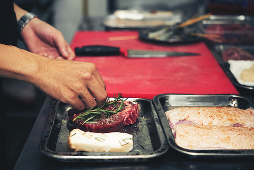 Hands of chef seasoning meat he is going to bake or grill