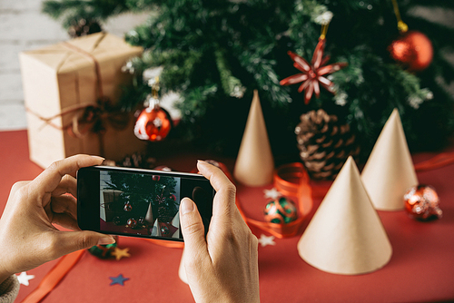Close-up of unrecognizable woman photographing Christmas composition against tree to post it on social media