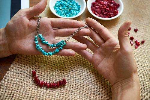 Close-up of female hands holding her hand worked necklace from natural stones, and she weaving the other one at the table