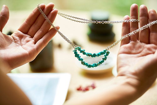 Close-up of female hands holding handmade necklace from gemstone beads on chain