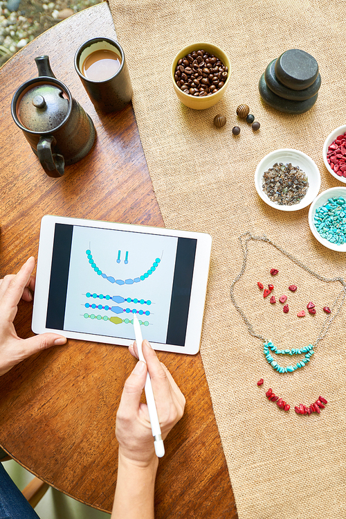 Woman sitting at the table and using the beading mobile app, she making her necklace handmade according to the sample