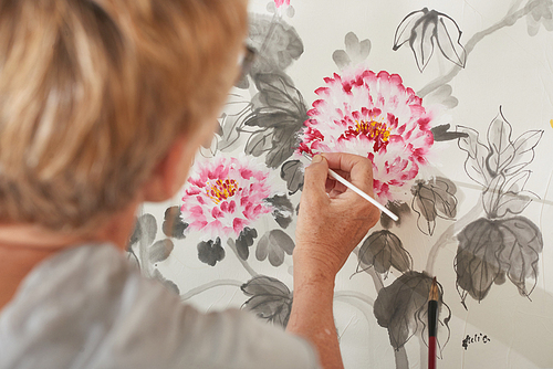 Aged woman painting flowers in art studio