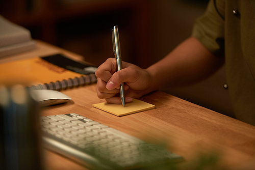 Close-up of hand making a note with pen on sticky paper