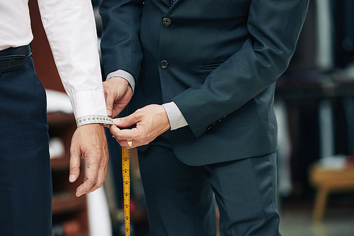 Cropped image of tailor measuring cuff of male client