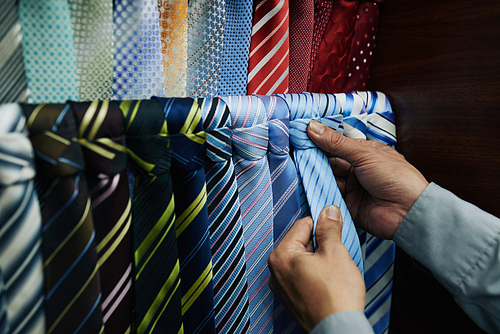 Hands of customer choosing perfect blue tie for his suit