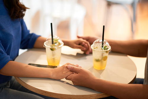 Couple holding hands when drinking fresh cocktails in cafe