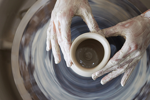Hands of person making jar out of clay, view from above