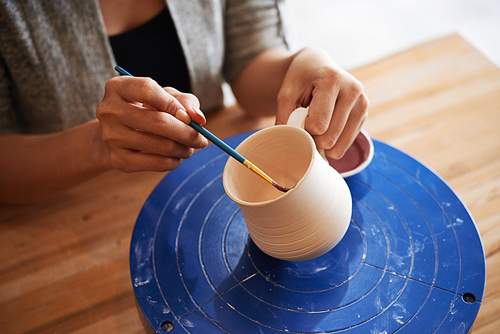 Hands of woman painting mug she made from the inside