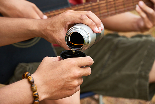 Hands of hiker pouring hot tea from thermos