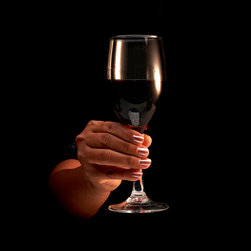 Close-up shot of hand of unrecognizable female holding glass of red wine on black background