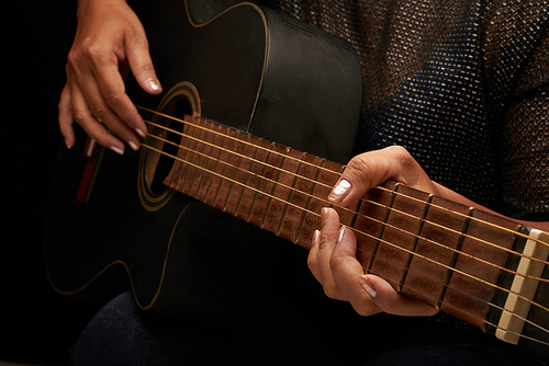Close-up shot of unrecognizable musician wearing blouse and jeans playing acoustic guitar, black background