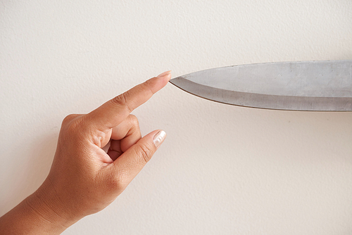 Close-up shot of unrecognizable woman touching tip of knife, isolated on white