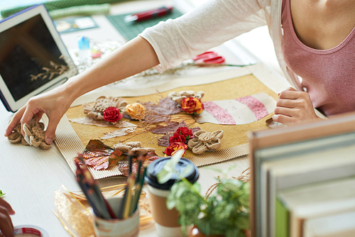 Gifted designer in casualwear sitting at desk of modern design studio and working on ambitious project with enthusiasm, she wrapped up in making decor item with withered and textile flowers