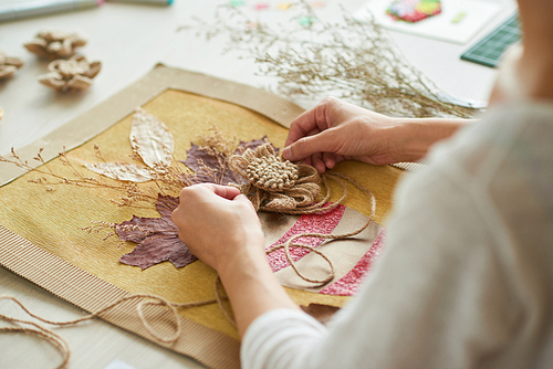 Close-up shot of talented woman sitting at desk and giving final touches on creative decor item