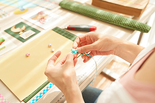 Close-up shot of unrecognizable woman sitting at living room and wrapped up in scrapbooking, decor items and tools lying on table