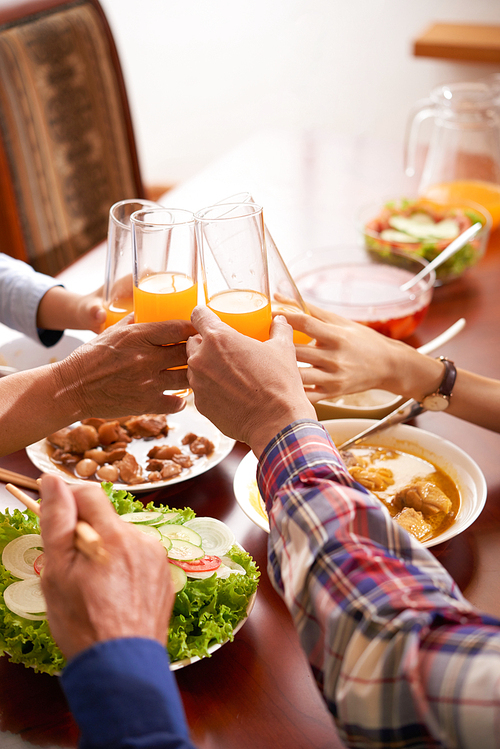 Hands of family memebers clinking glasses of orange juice over dinner table