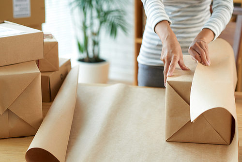 Woman wrapping box with present or product to ship it