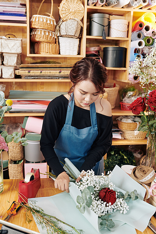 Asian female florist wrapping beautiful bouquet in decorative paper