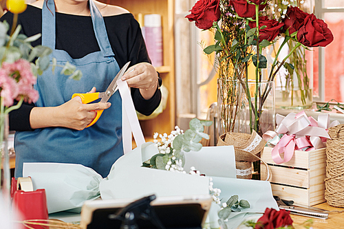 Cropped image of florist cutting decorative ribbon when working on bouquet