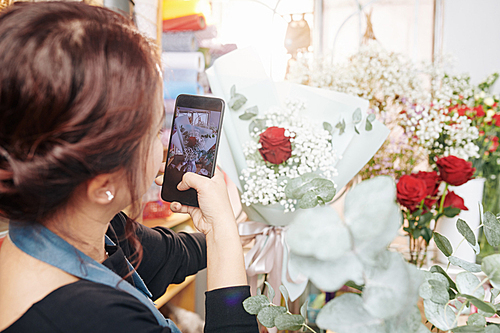 Florist using smartphone to take photo of bouquet she made and upload it on social media