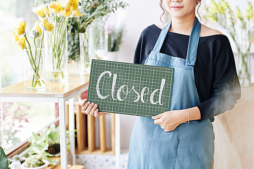 Cropped image of young female shop owner holding plastic board with closed inscription