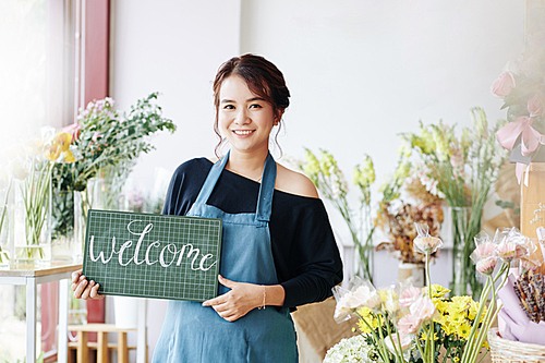 Pretty smiling young Vietnamese florist inviting customers to her new small flower shop