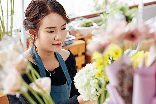 Young lovely Vietnamese florist in blue apron working at flower studio